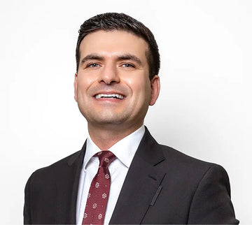 Dr Ehsan Azimi in a dark suit, white dress shirt, and a burgundy patterned tie, photographed against a plain light background.